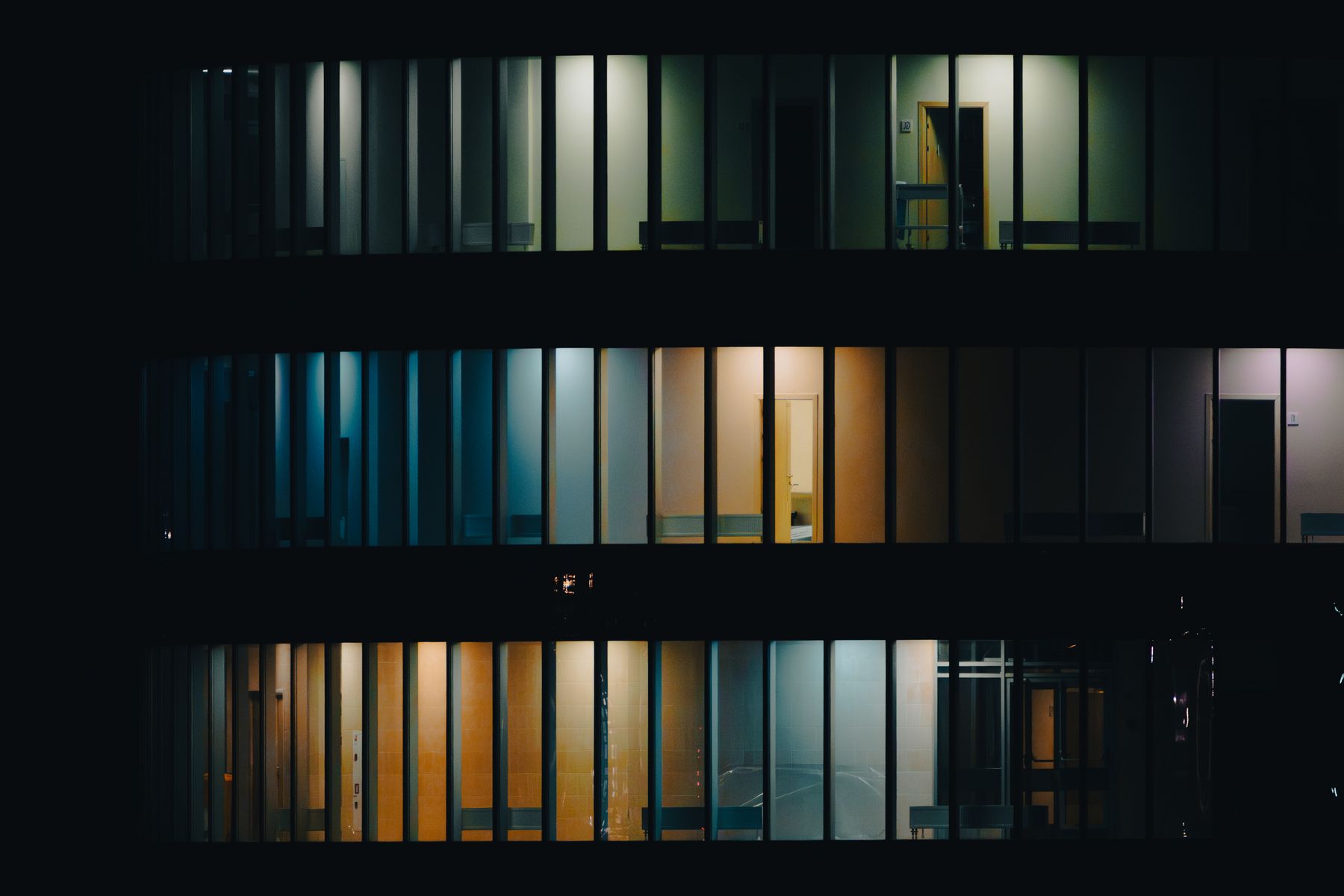 Illuminated office windows and interior rooms visible across a dark building facade at night.