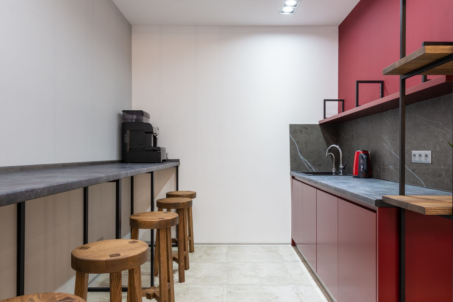 Office kitchenette with red cabinets, a sink, small appliances and wooden stools along a counter.