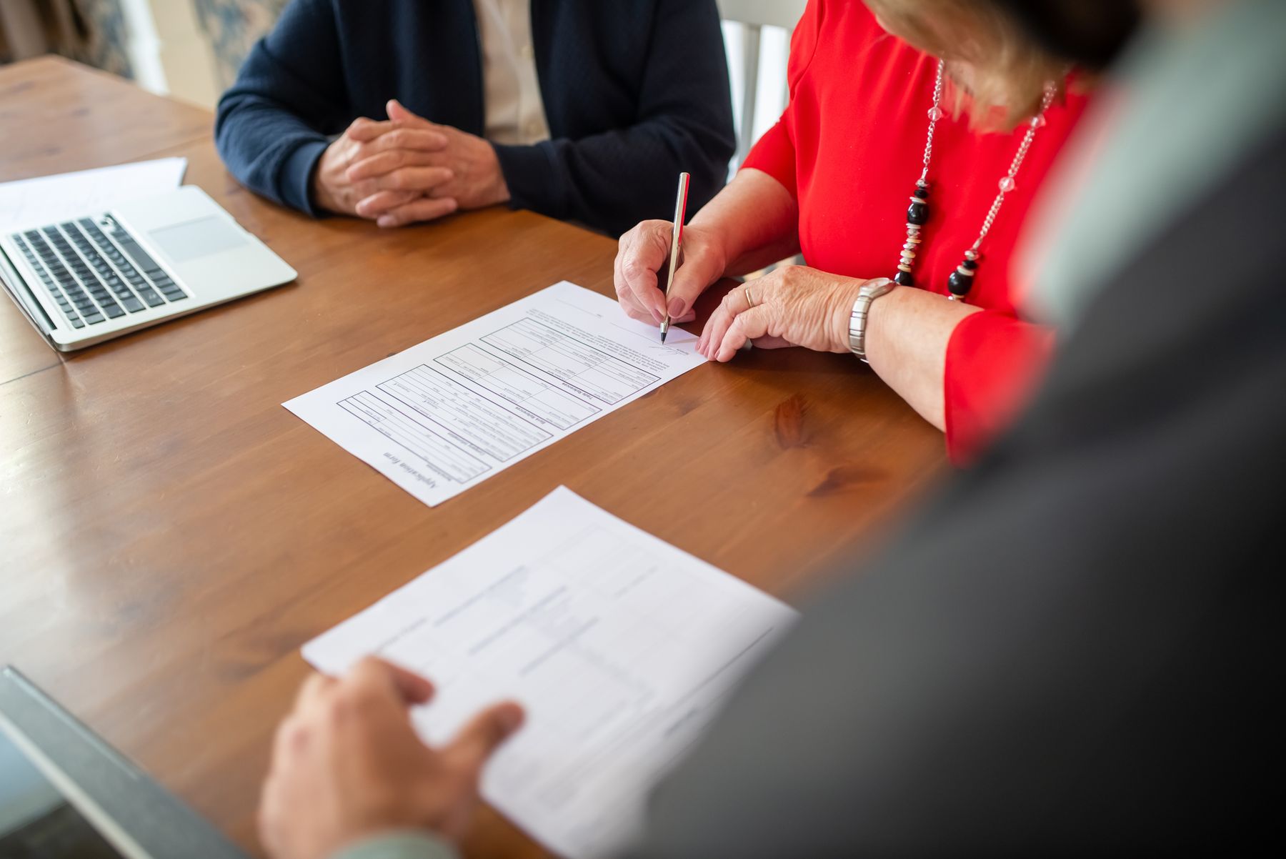 A woman signs paperwork at a wooden conference table with other meeting participants.