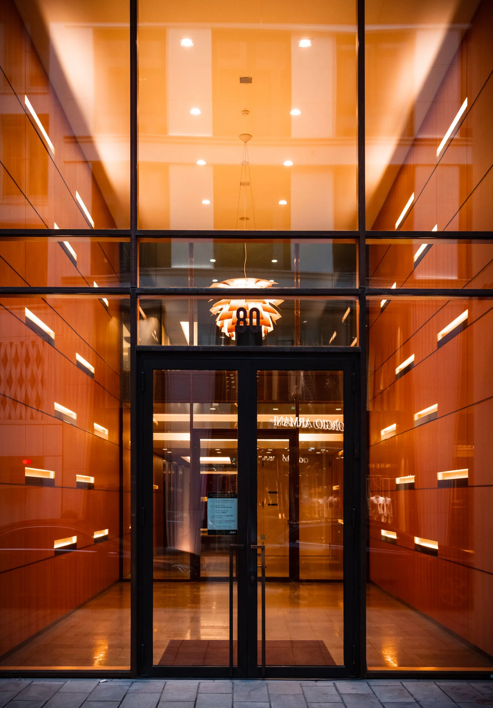 Glass entrance doors beneath a tall glazed canopy with warm interior lighting.