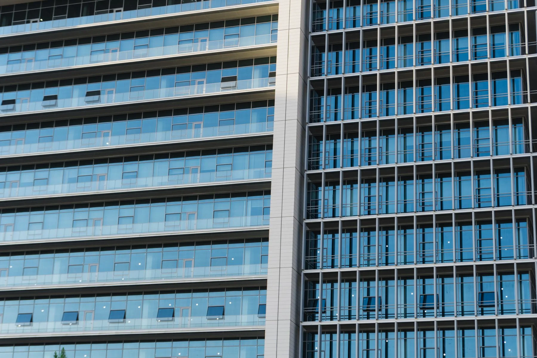 Adjacent sections of a modern office facade with rows of windows, balconies and metal louvers.
