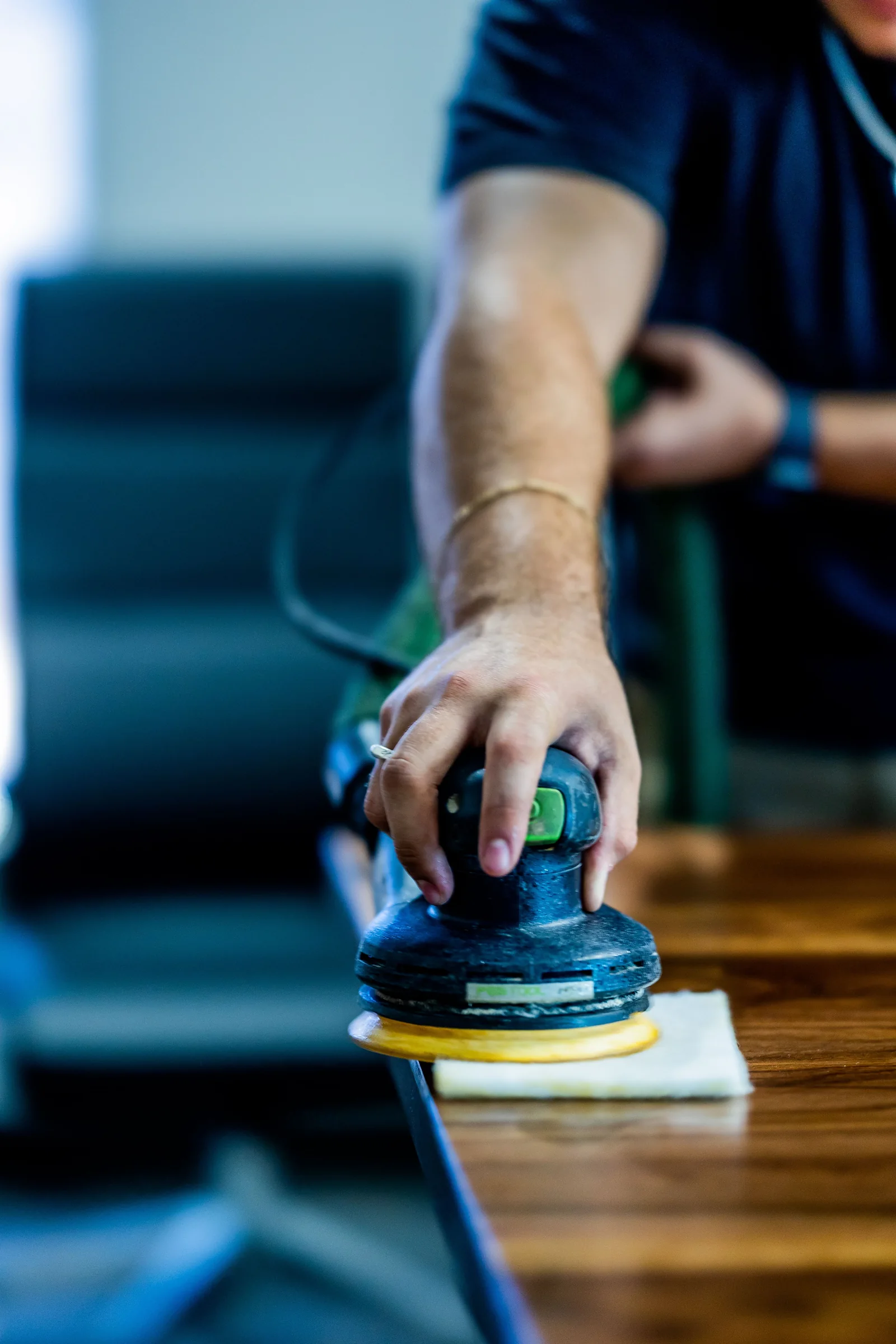 Worker using a handheld polishing pad on a wooden tabletop. Photo by Caleb Oquendo, Pexels.